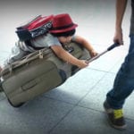 child wearing backpack riding on suitcase