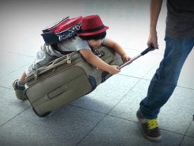 child wearing backpack riding on suitcase