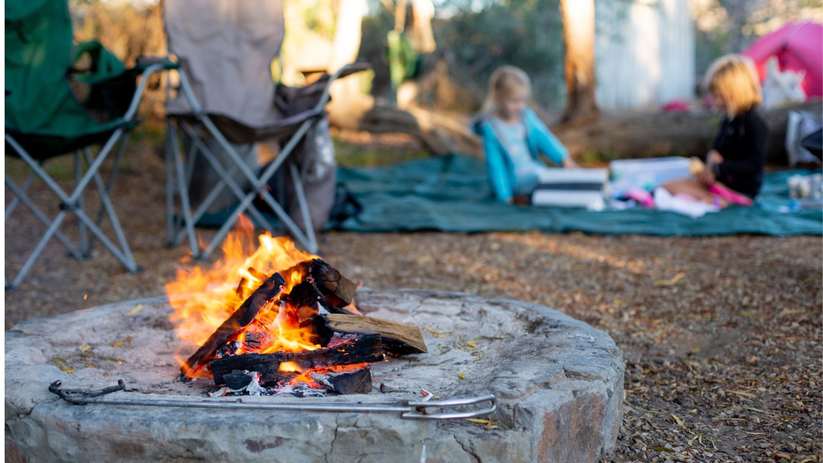 camp fire with kids playing on a blanket 10 feet away