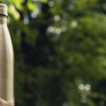 silver travel water bottle sitting on a bench in a forest