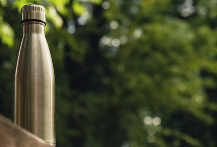 silver travel water bottle sitting on a bench in a forest