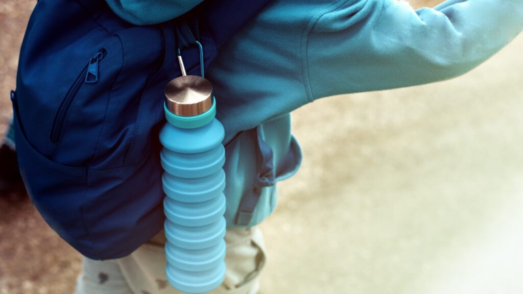 person with a collapsible water bottle attached to their backpack