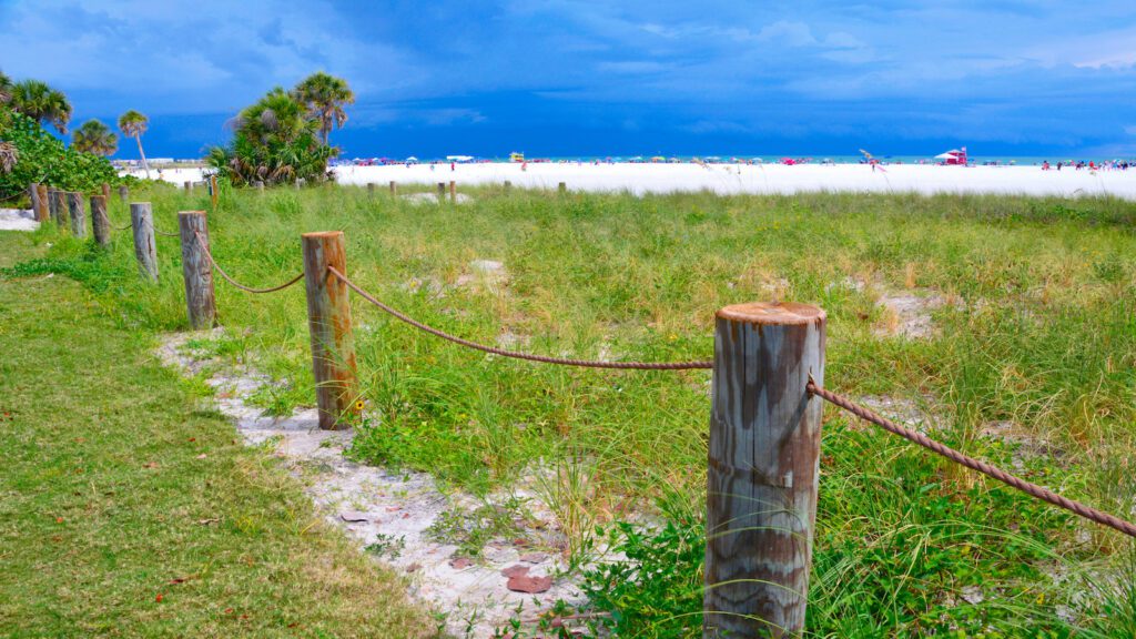 Grassy area roped off from beach with white sand and water in the distance