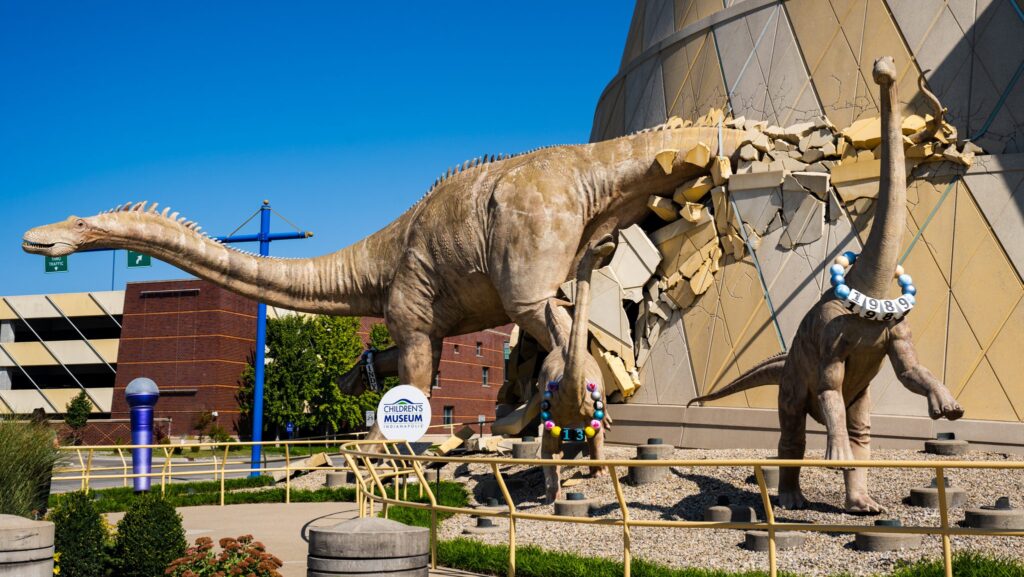 Two dinosaurs wearing friendship bracelets outside the Children's Museum of Indianapolis