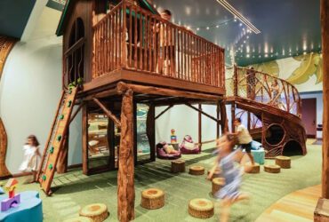 Kids running around a treehouse play structure inside a building