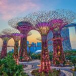 Futuristic buildings and colorful structures in a tree-lined park at sunset