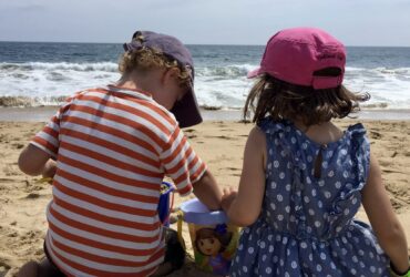 two children sitting on a beach digging in the sand with a bucket