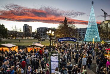 A evening view of the Denver Christkindlmarket with wooden booths and a lighted Christmas tree