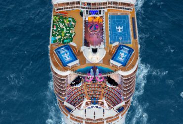 Top deck of cruise ships sailing in ocean, with a sports court, slide, surf simulators, and other features