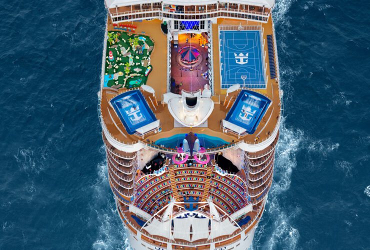 Top deck of cruise ships sailing in ocean, with a sports court, slide, surf simulators, and other features